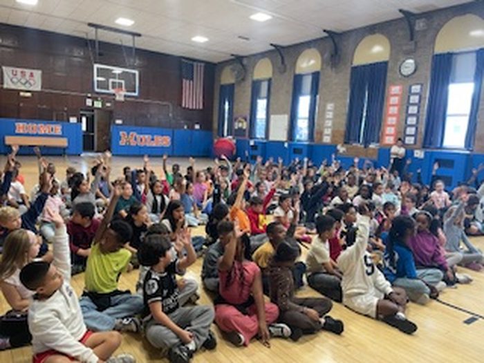 Students raising their hands to answer questions during the assembly