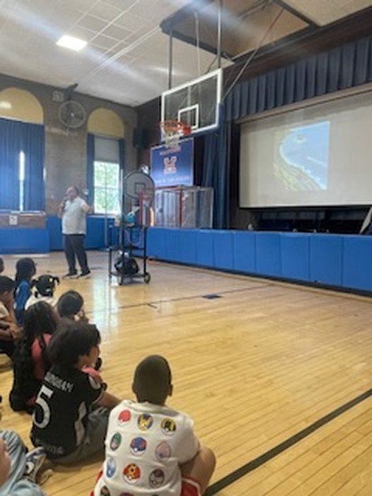 Edward Rodriguez sharing another illustration from the book with students seated on the gym floor
