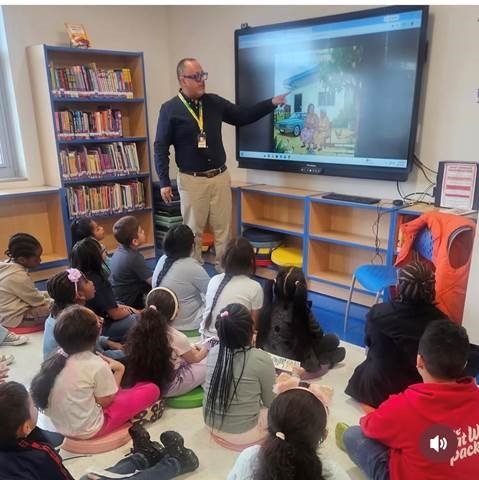 Edward Rodriguez pointing to a farmhouse illustration from the book on the classroom screen