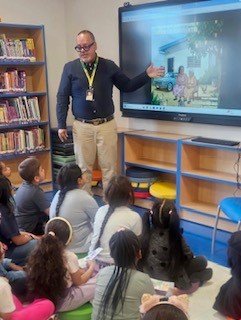 Edward Rodriguez presenting to second graders seated on the library floor